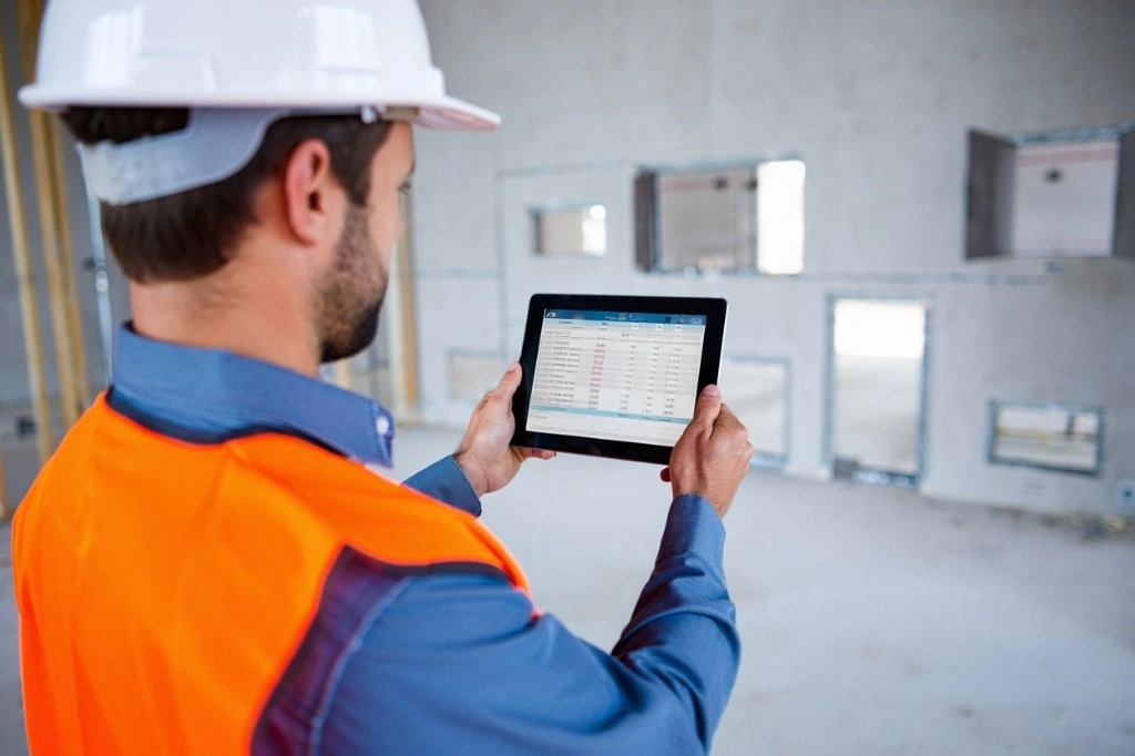 A construction manager using a tablet to calculate the cost impact of a drywall access panel installation at a job site.