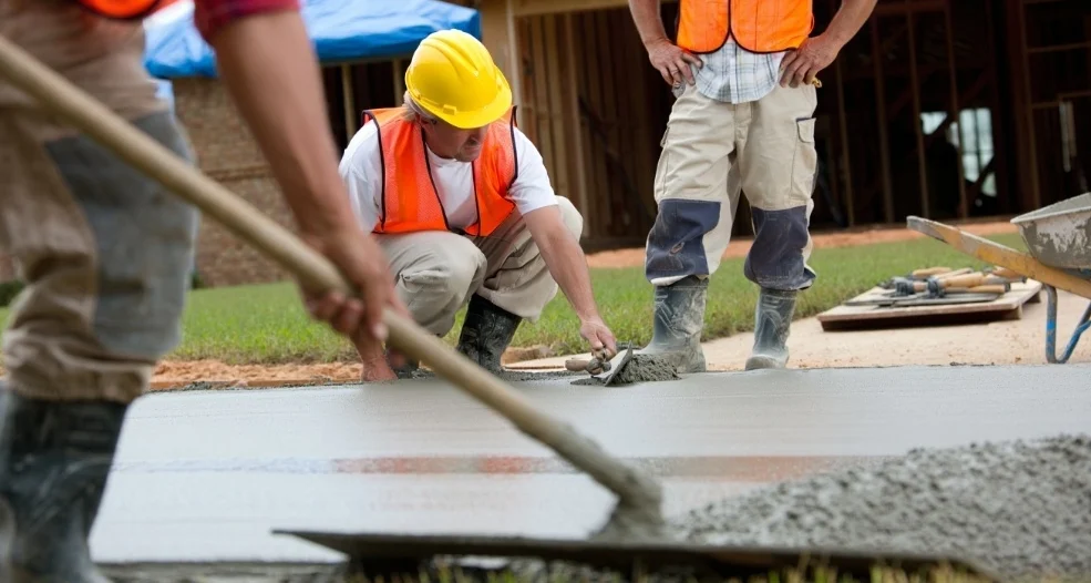 Construction crew leveling wet cement to estimate the total price of concrete per yard for a residential patio.